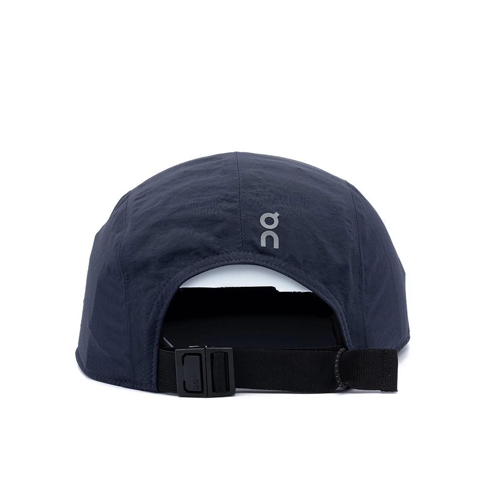 The back view of a dark navy blue On running cap with an adjustable black strap and a small white 'on' logo on the side, set against a plain white background.