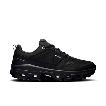 Side view of the women's On Cloudrock Low Waterproof in black, showing the lace-up upper and chunky lugged sole.