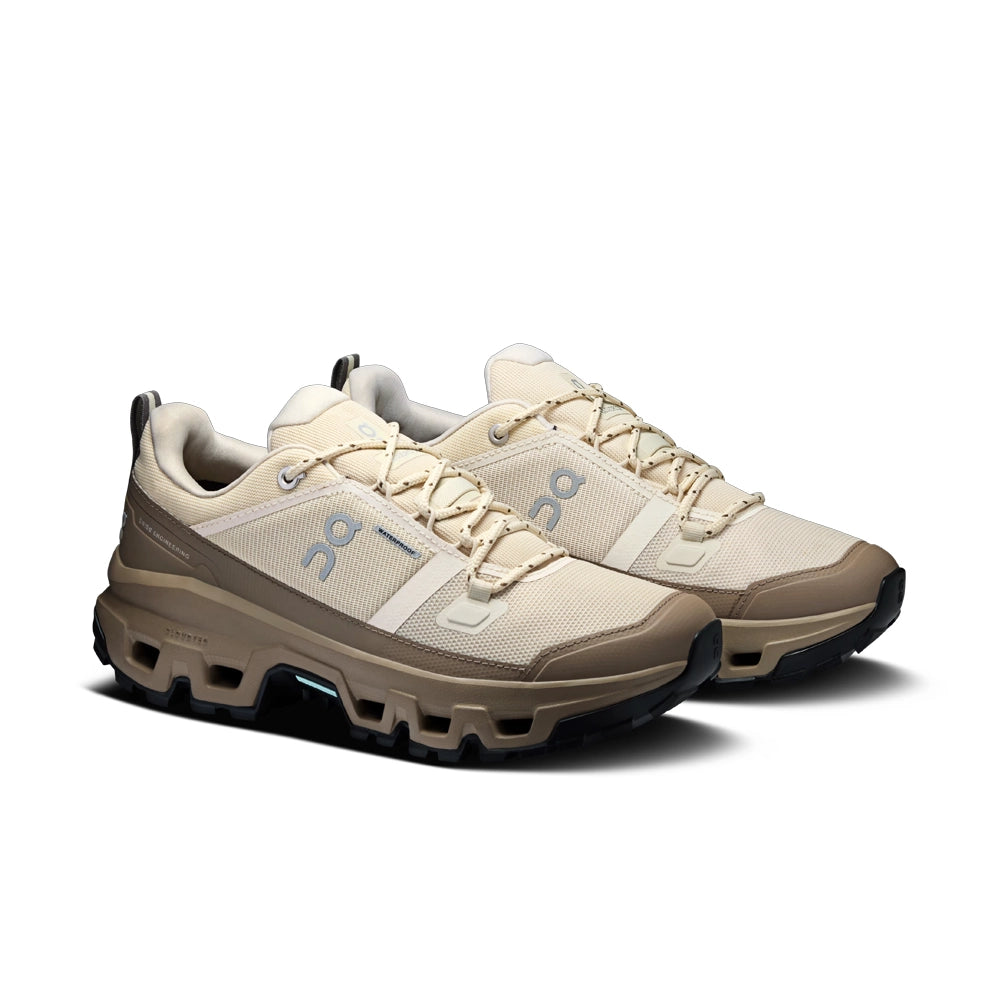 Pair of On women's Cloudrock Low Waterproof shoes in Grain Soba, angled front view showing cream laces and grayish-brown toe guards.