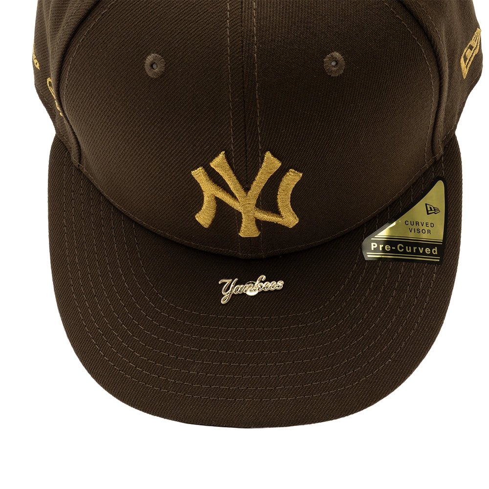 Close-up of gold NY embroidery and Yankees script pin on the walnut brown cap's curved visor.