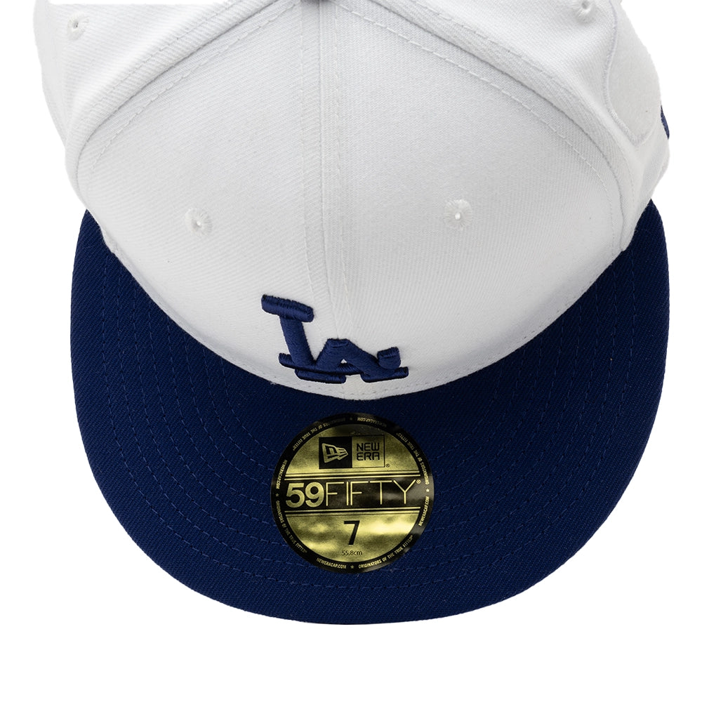 Overhead close-up of the white Dodgers cap showing the navy LA embroidery, navy brim, and gold 59FIFTY sticker.
