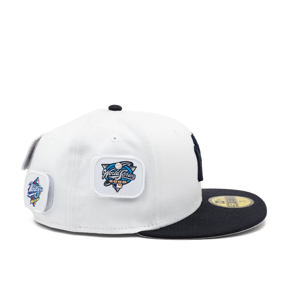 Side view of the white Yankees fitted cap with a 2000 World Series patch and additional patches toward the back.