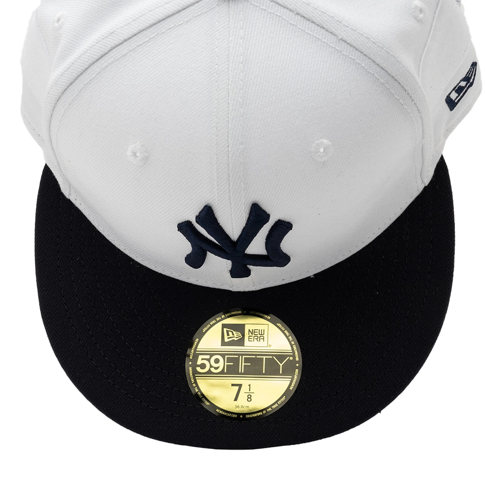 Top-front close-up of the white Yankees 59FIFTY cap showing navy NY embroidery, a navy brim and a gold size sticker.