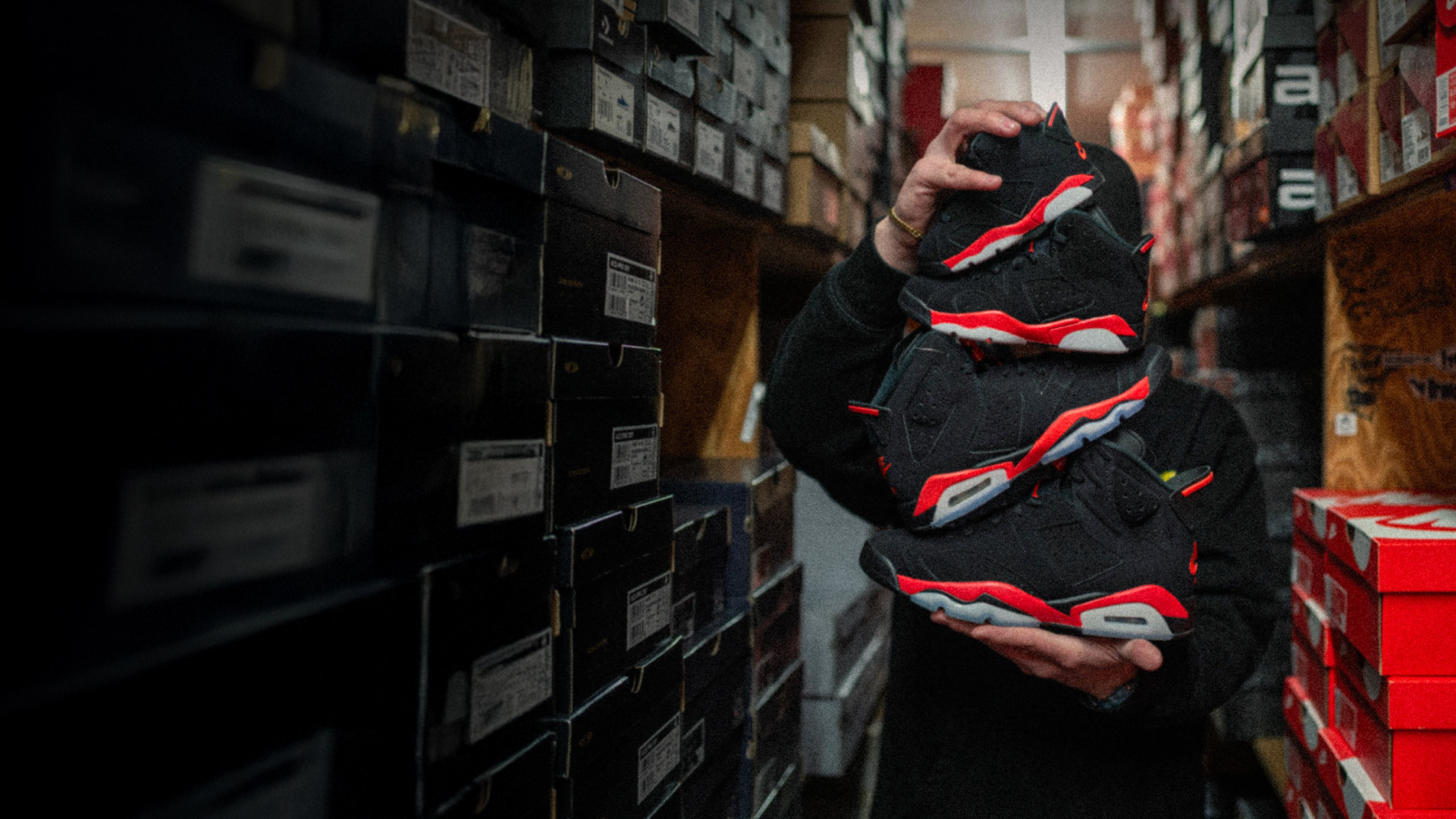 Person holding a black and red sneaker in a warehouse setting - Air Jordan 6 Retro 'Infrared Salesman'slider_item_BhGJ4y