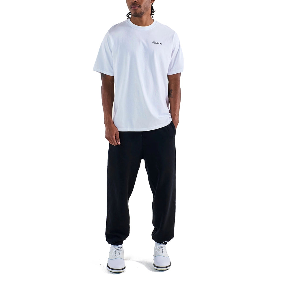 Model wearing a white Malbon Bermuda Baldwin T-shirt with a chest logo, black pants, and white sneakers