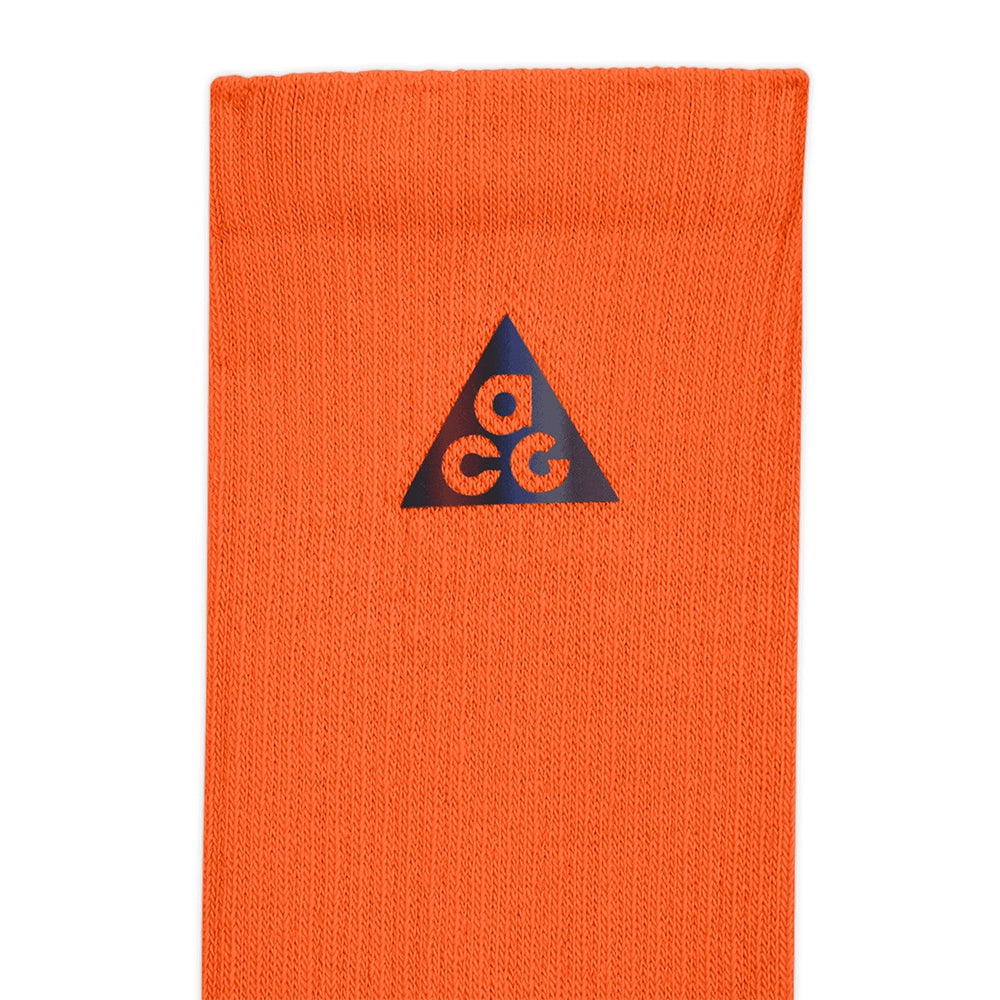 Close-up of the black triangular ACG logo on the ribbed Safety Orange Nike crew sock.