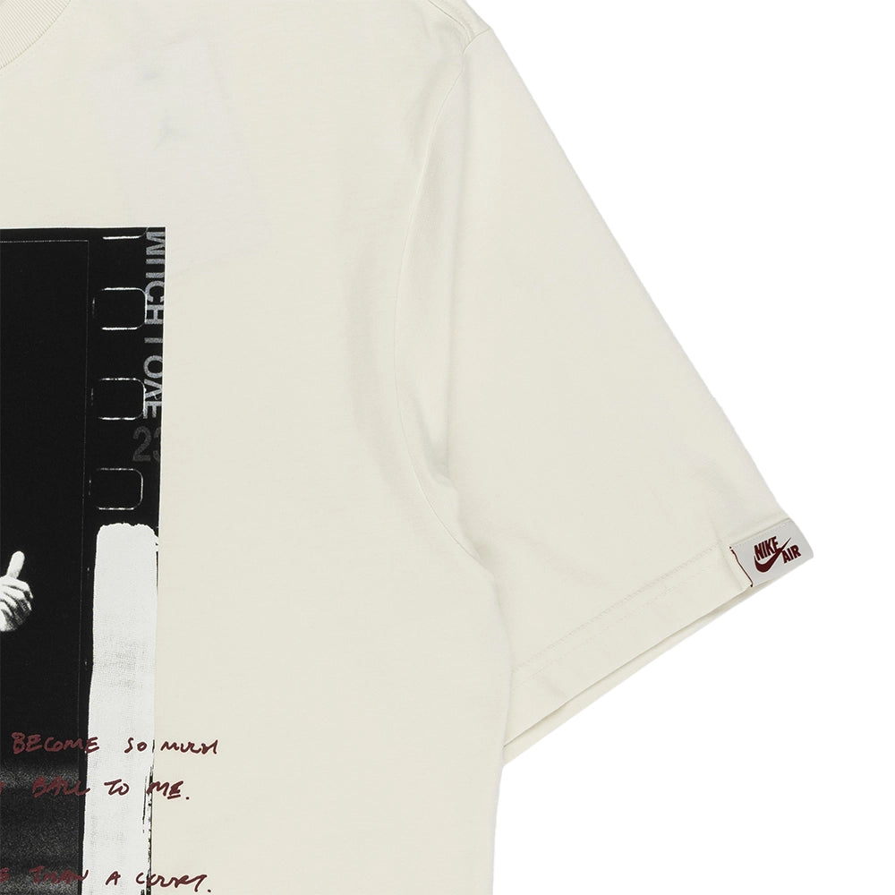 An off-white short-sleeve t-shirt featuring a black and white graphic print on the front and a small red Nike Swoosh logo on the sleeve cuff.