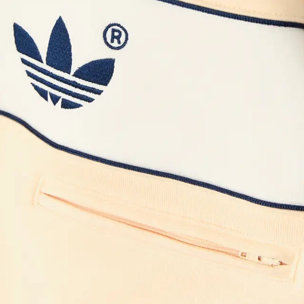 Close-up of the navy Trefoil logo and concealed zip pocket on the adidas Warm Vanilla hoodie.