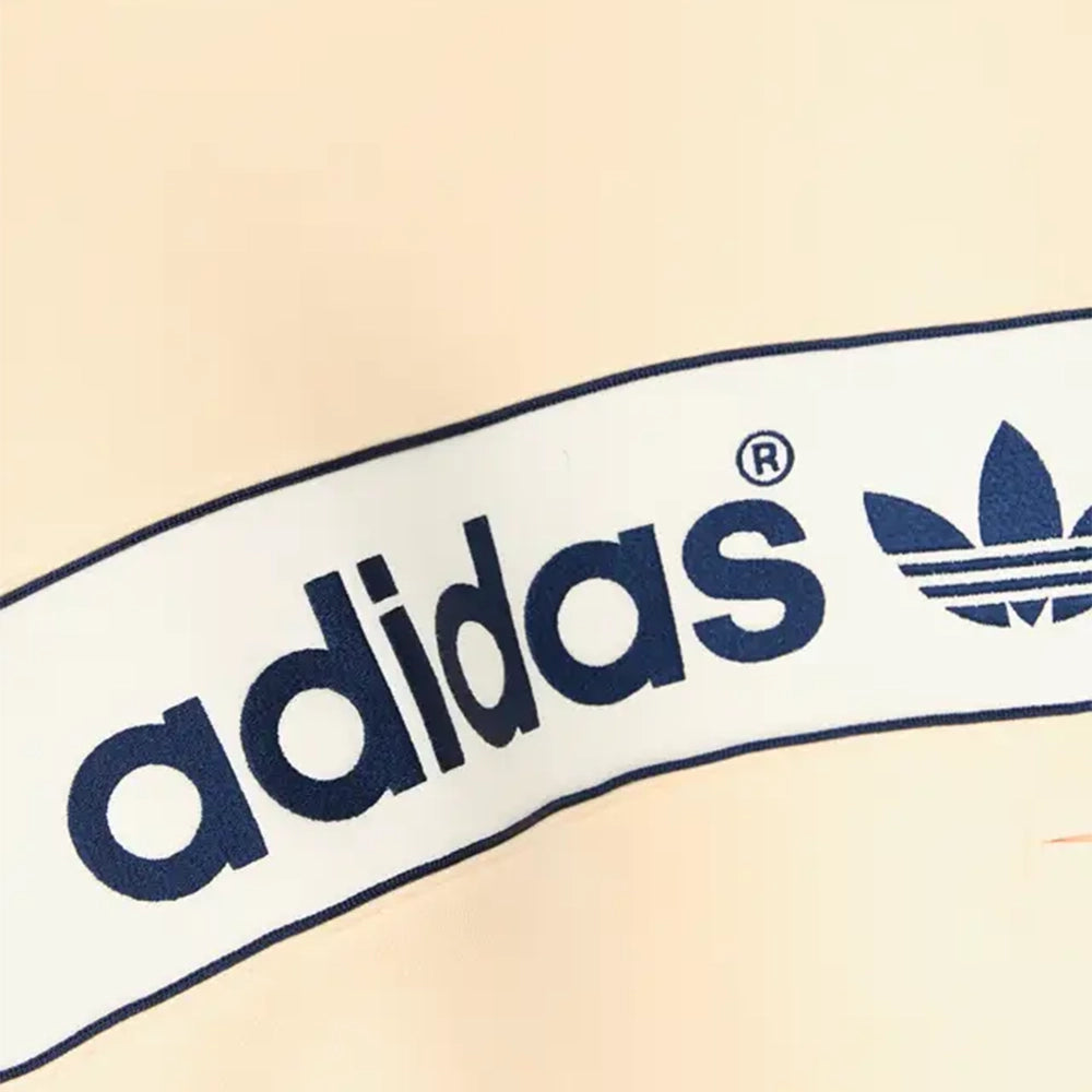 Close-up of navy adidas lettering and Trefoil logo on the cream chest panel of the Warm Vanilla hoodie.
