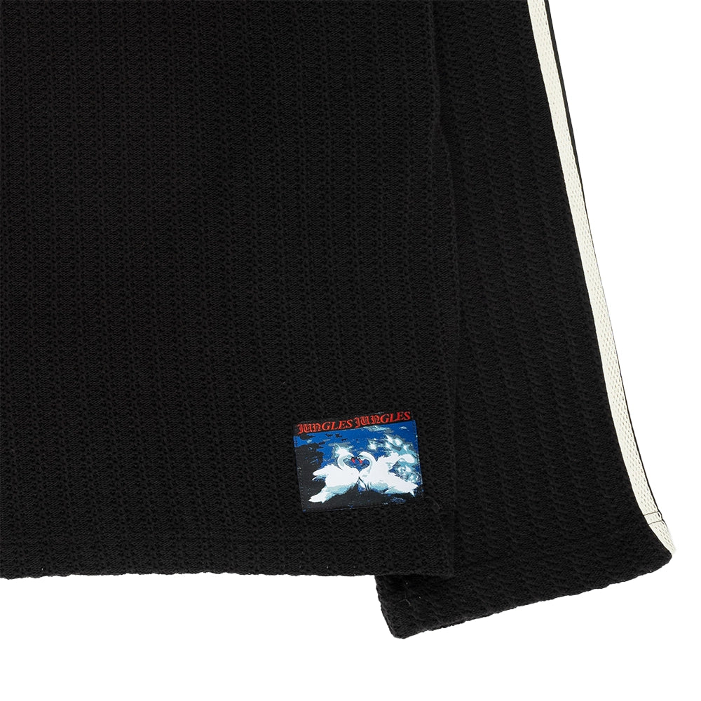Close-up of a black textured knit garment, likely a sweater or scarf, showing a small colorful embroidered patch and a blue-and-white illustration.