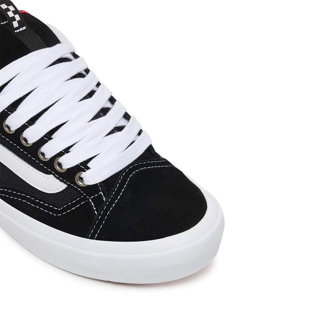 Close-up of a black and white low-top sneaker, showing the black canvas upper, white laces, metal eyelets, and white rubber sole on a white background.